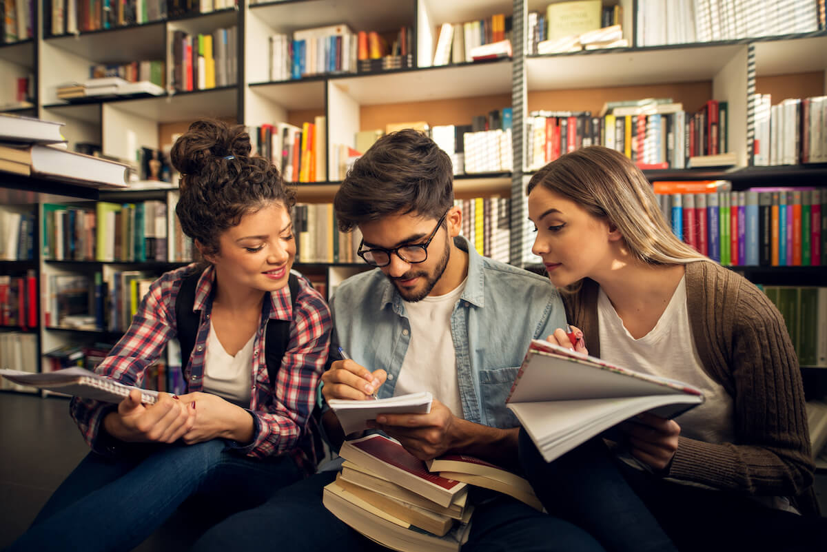 A group of high school students sitting on the floor in the library working on an assignment