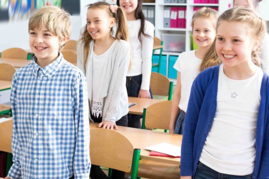 Young students standing in front of their desks in a classroom