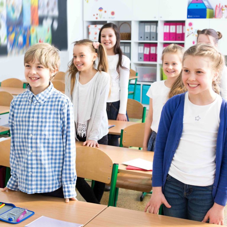 Young students standing in front of their desks in a classroom