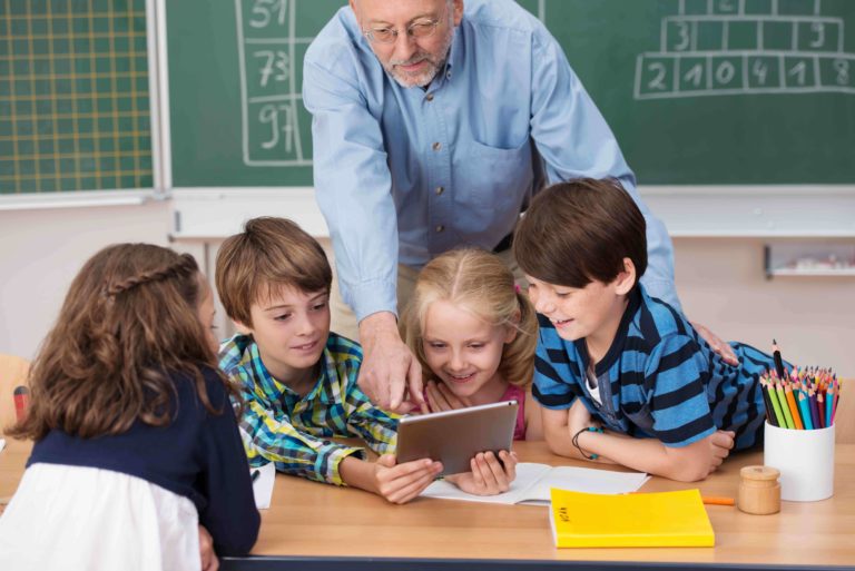 Male teacher and young children hovered over a tablet