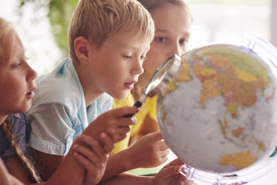 Young kids holding a magnifying glass and looking at a globe