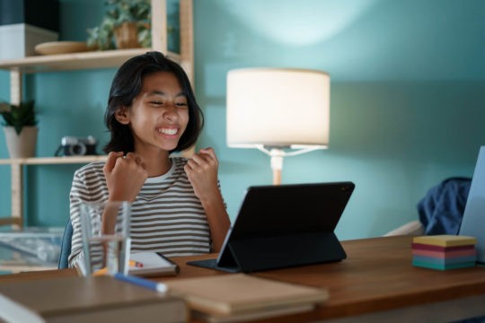 Young girl smiling and excited while looking at a tablet.