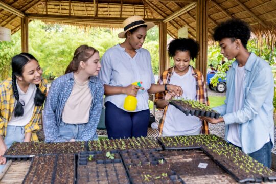 A group of students standing with their teacher, learning about plants on a farm.