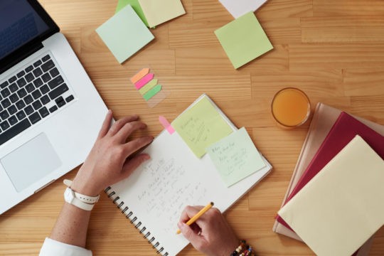 Woman working on a laptop and making notes in a notebook.