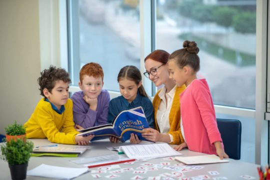 Teacher sitting with young children working on English grammar.