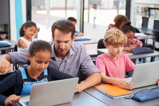 Male teacher helping young female student at laptop