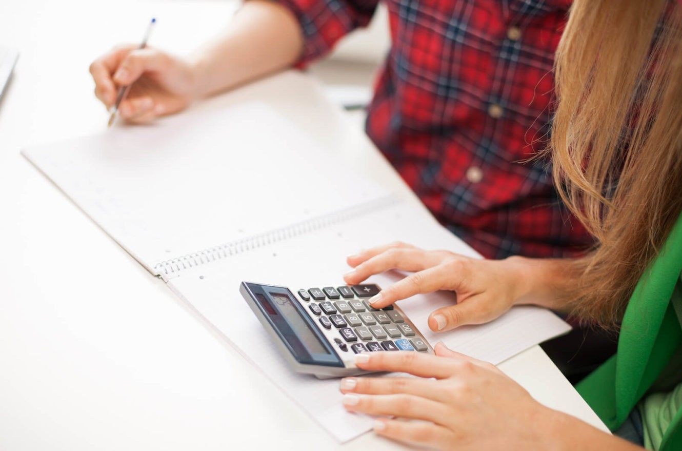 Two high school students working out a math problem with calculator and paper