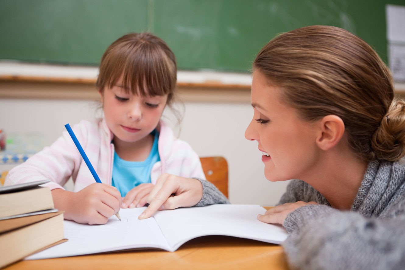 Female teacher working with young student who is writing in her notebook