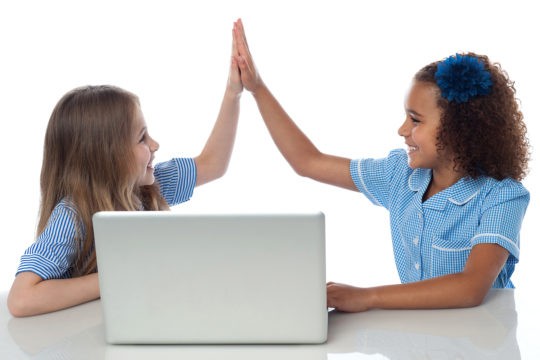 Two young girls high fiving in front of laptop