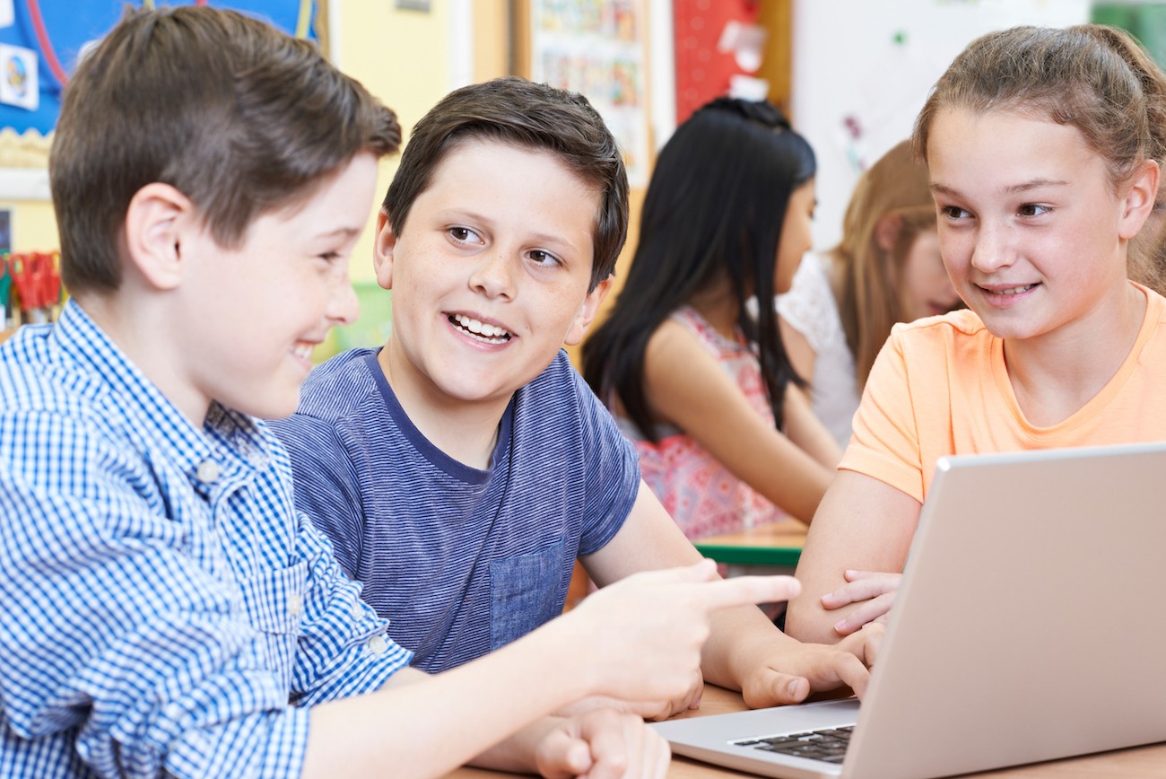 A group of young students talking in front of a laptop