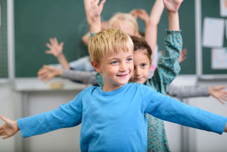 Group of young students standing in a line in a classroom stretching their arms.