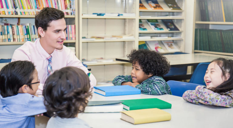 Group of young students sitting at a table in the library with a teacher.