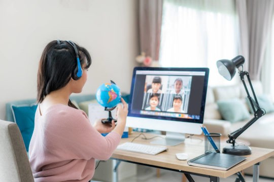 Female teacher pointing to a globe while in a zoom class with a small group of students.