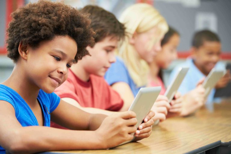 Young students sitting at desks looking at tablets