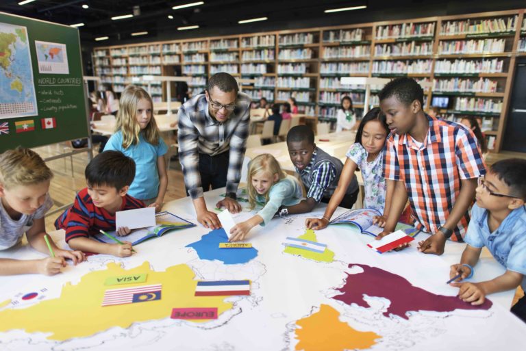 Teacher with a group of young students identifying continents on a map in the library.