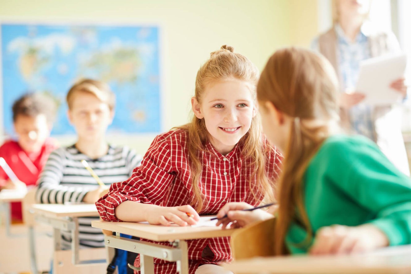 Two young girls talking at their desks in class