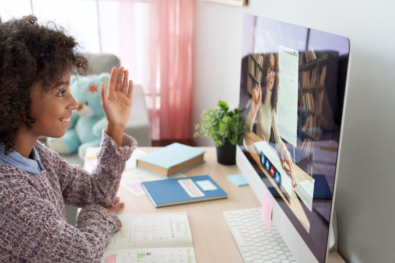 Smiling girl sitting at a desk with a computer participating in a Zoom class.