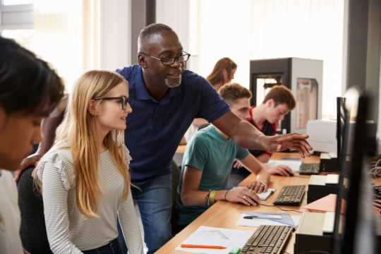 Older teacher helping a student working on a computer.