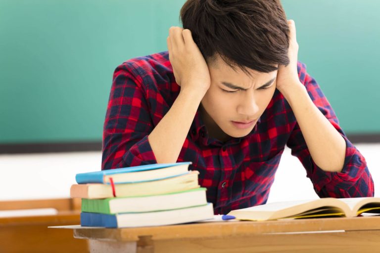 Older student sitting at a desk in a classroom struggling with reading a book.