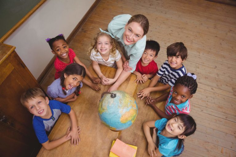 Diverse group of young students and their teacher sitting around a table with a globe.