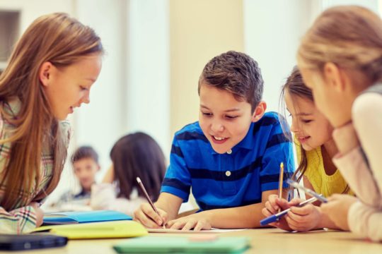 Group of young students sitting at a table working on a worksheet together.