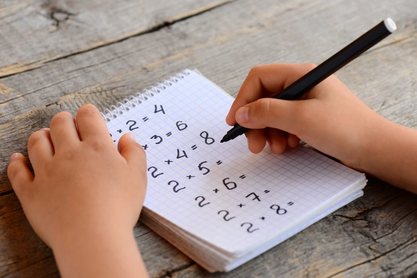 Young boy writing multiplication problems on a notepad