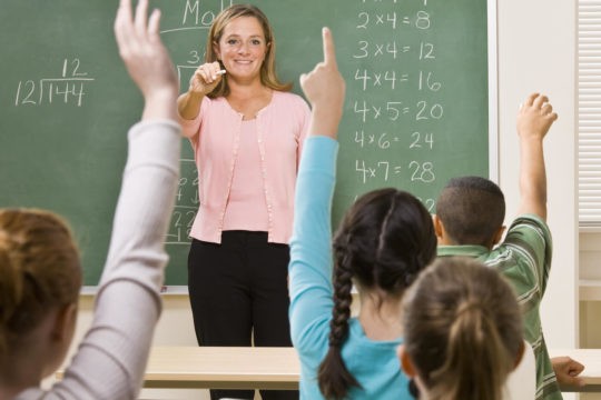 Math teacher at the front of the classroom calling on students.