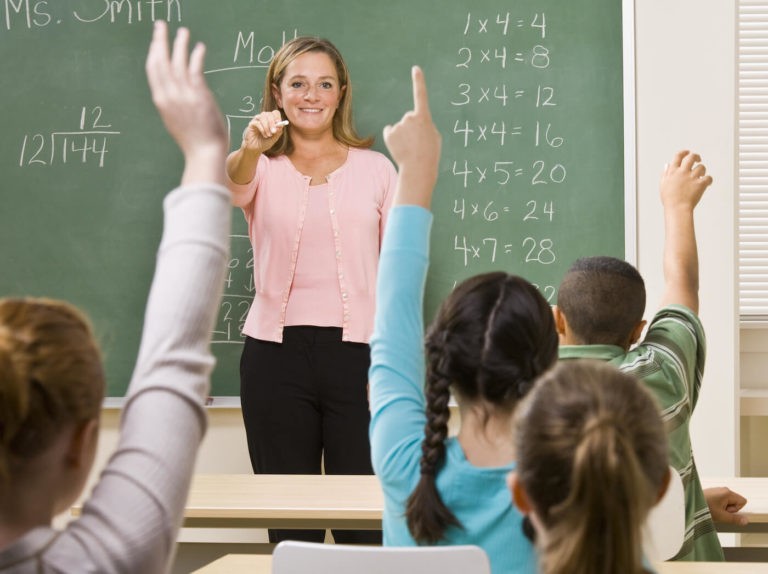 Math teacher at the front of the classroom calling on students.