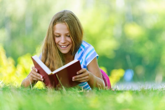 Smiling girl lying in the grass reading a book.