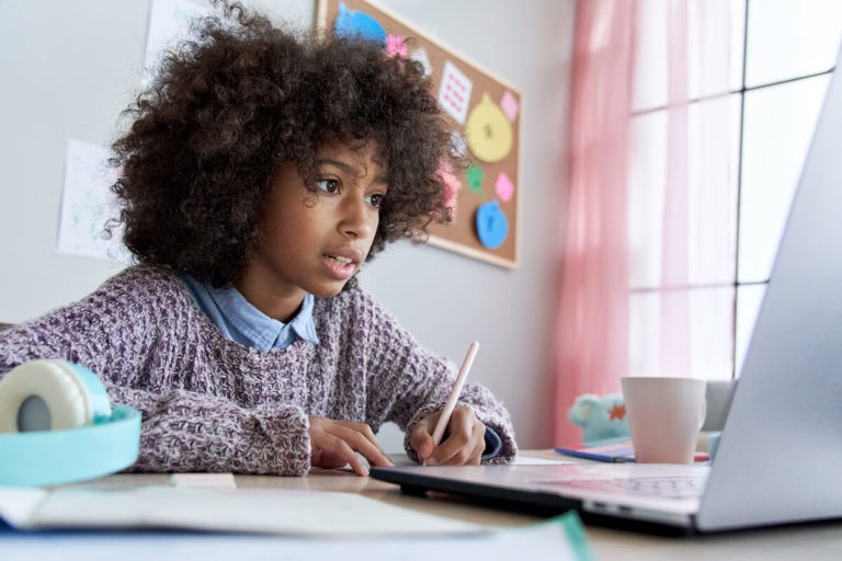 Young girl taking notes while watching something on her laptop.