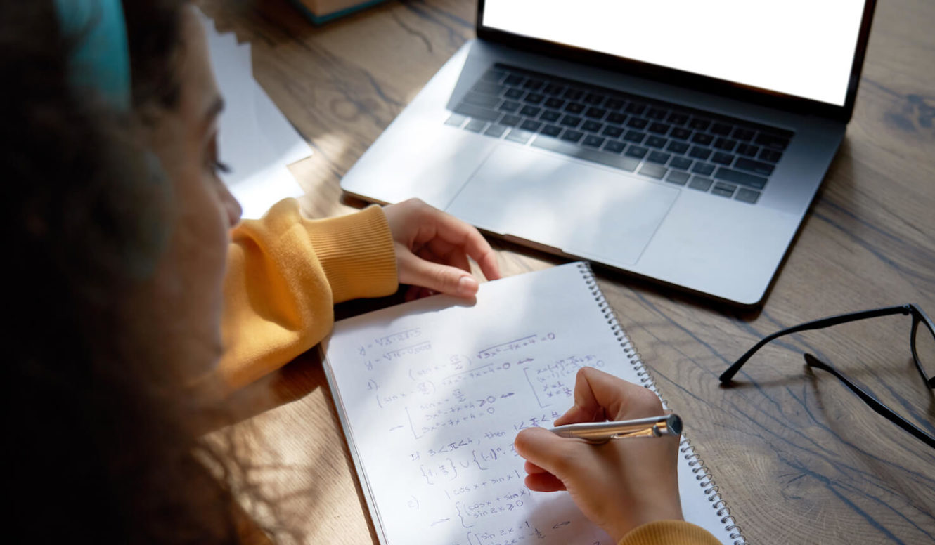 Female high school student working out math problems on notebook with laptop