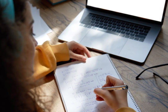 Female high school student working out math problems on notebook with laptop