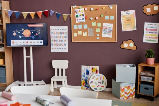 An organized classroom has a colorful focus wall hung up on the wall.