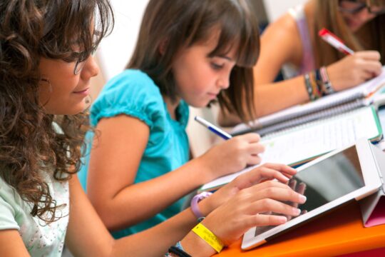 A group of teenage girls does homework on their notebooks while one uses a tablet.