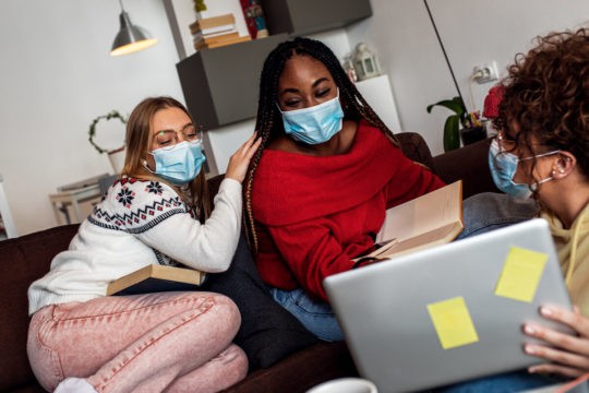 A small group of older students wearing masks and working together on a laptop.