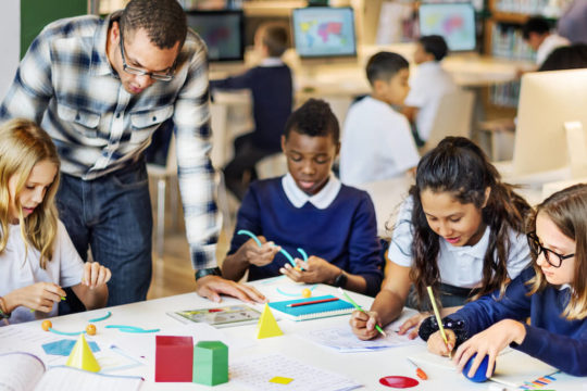 Group of young students sitting a table using manipulatives.