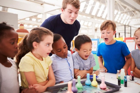 Group of young students gathered around a science experiment.