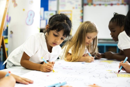 Young students drawing and sitting at a table.