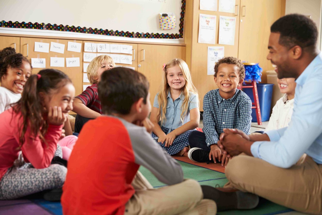 A group of young students sitting quietly on the floor with their teacher