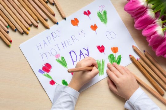 Child drawing a rose on a Mother’s Day Card.