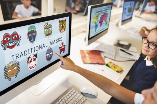 Student pointing to a computer with images of traditional masks.