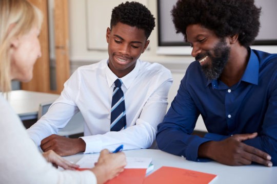 Boy and father meeting with a teacher in a classroom.