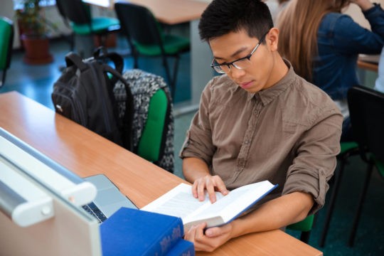 A male student reads a book in a classroom.