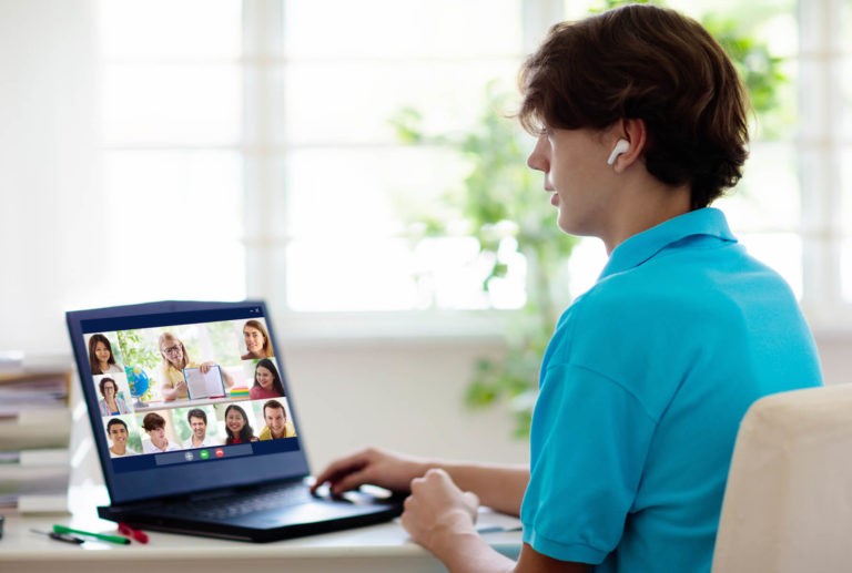 Teenage boy sitting at a desk participating in a virtual learning classroom.