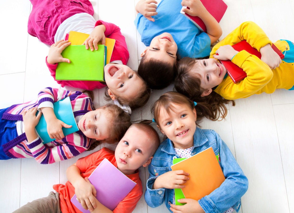 A group of smiling children laying on the ground in a circle holding books