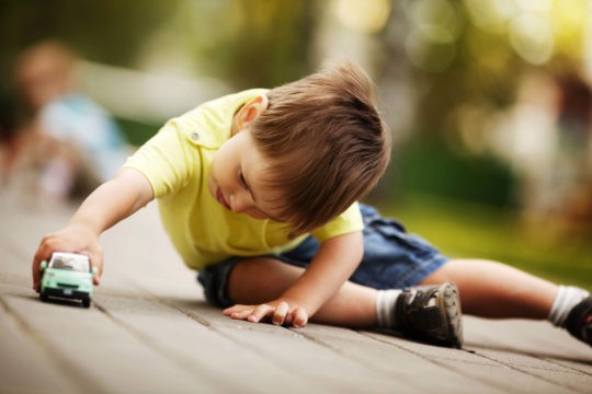 Little boy playing outside with a toy car