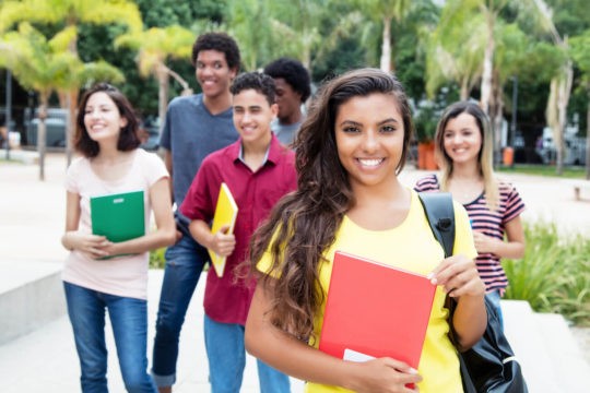 A group of multiracial high school students holding books and smiling