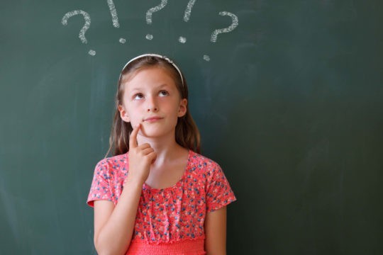 Young girl standing in front of a chalkboard thinking