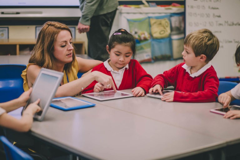 Teacher helping a young student working on an iPad.