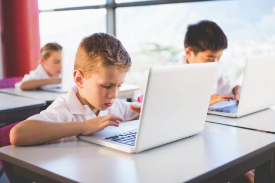 Young students sitting at their desks working on laptops.